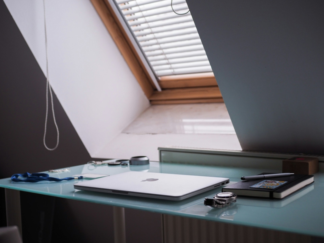 Bureau onder een schuin dakraam met gesloten jaloezieën, waardoor gedempt licht de kamer binnenvalt.