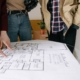 Twee mensen overleggen met een vakman over de plattegrond en bouwplannen van een huis