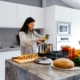 Een vrouw bereidt een maaltijd op een stijlvol keukenblok, omringd door verse ingrediënten en felgekleurde kookgerei in een moderne keuken.