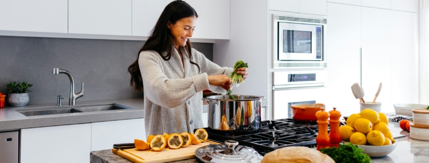 Een vrouw bereidt een maaltijd op een stijlvol keukenblok, omringd door verse ingrediënten en felgekleurde kookgerei in een moderne keuken.