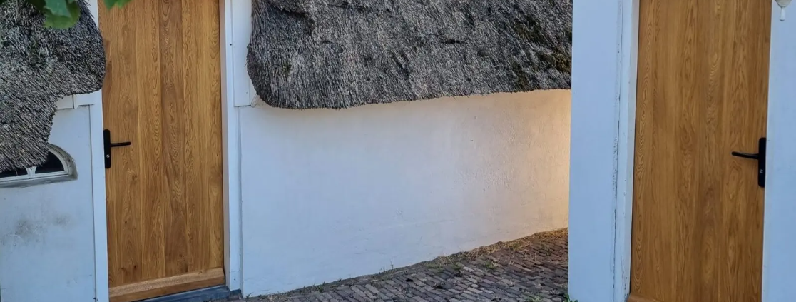 Traditioneel huis met houten voordeur en uitstekende isolatie, omgeven door een met riet bedekt dak en een geplaveide oprit.